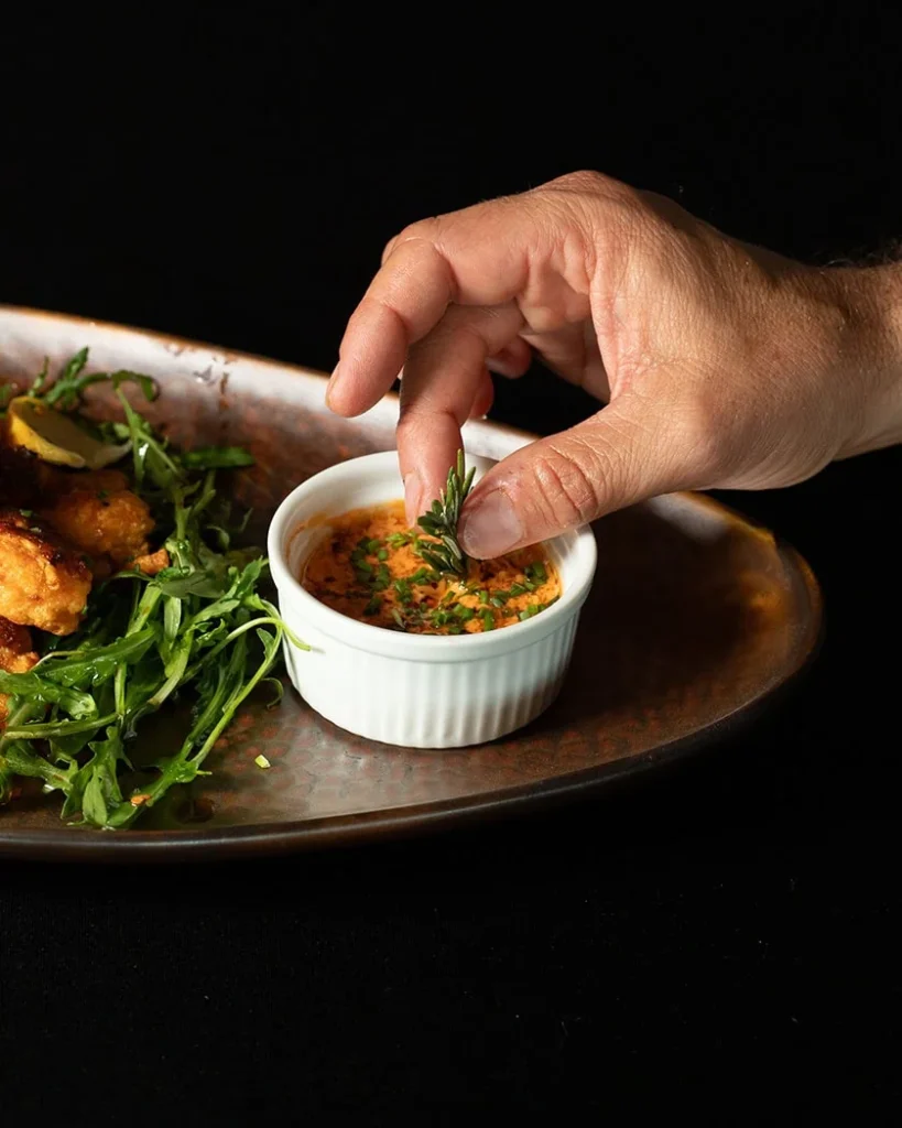 Mano decorando una salsa gourmet con hierbas sobre un platillo elegante en evento gastronómico